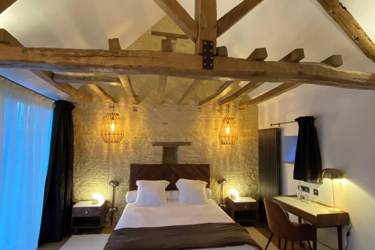 A bedroom with a wooden ceiling, a bed, bedside tables, a desk, and a chair.