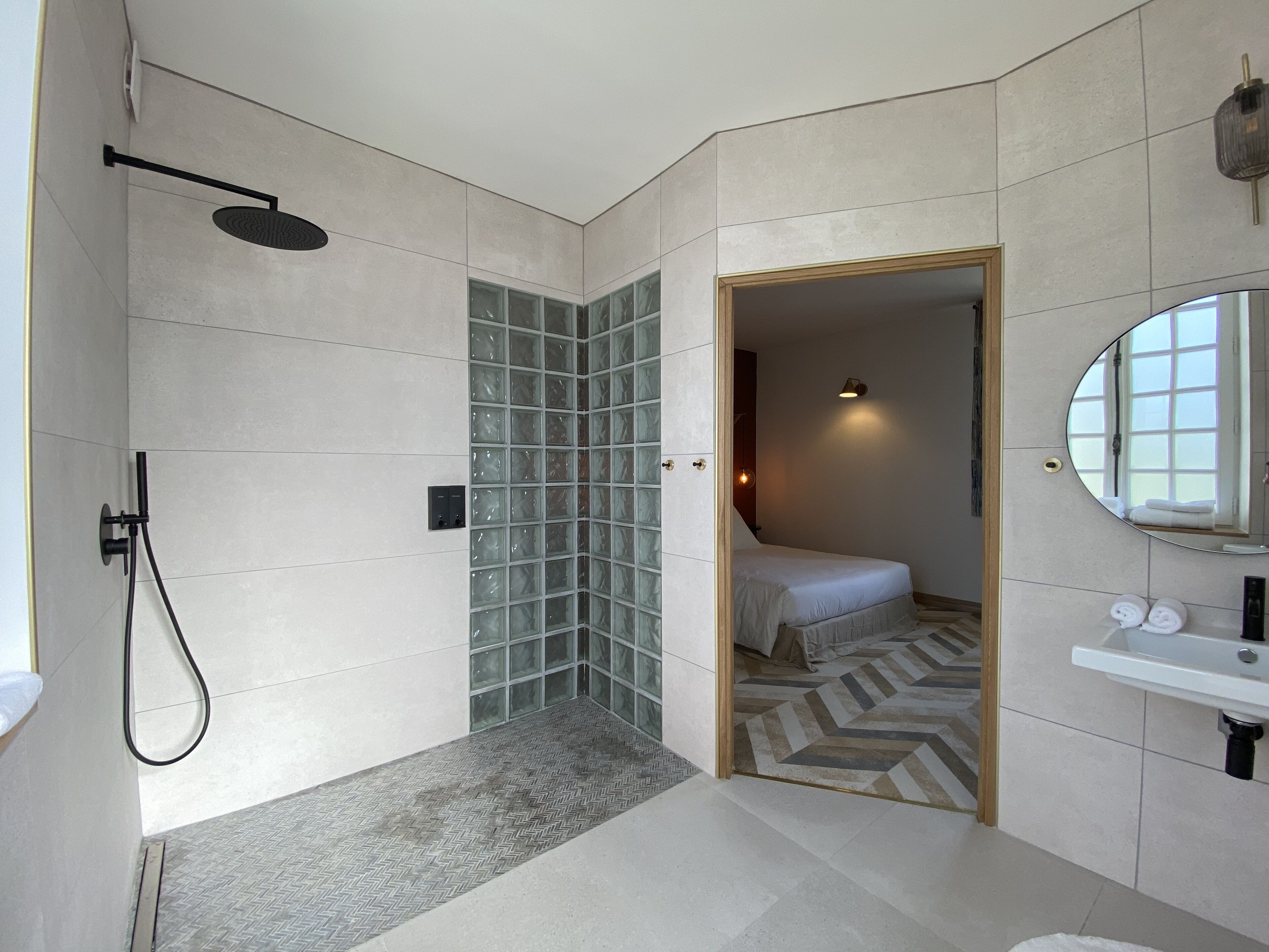 A modern bathroom with a shower, a glass block wall, a bed, and a sink.