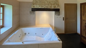 Un baño moderno con una bañera independiente, pared de piedra y un travesaño de madera.