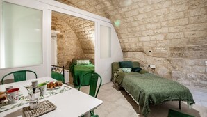 Una habitación con pared de piedra, cama con ropa de cama verde, una mesa con productos para el desayuno y una silla verde.