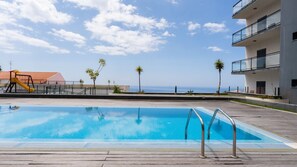 Una piscina amb un tram de fusta, un tobogan i vista a l'oceà.