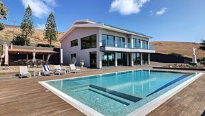 Ett modernt hus i två våningar med en swimmingpool, utemöbler och en grillplats.