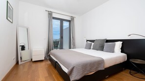 Een moderne slaapkamer met een bed, nachtkastje, raam met gordijnen en uitzicht op de stad.