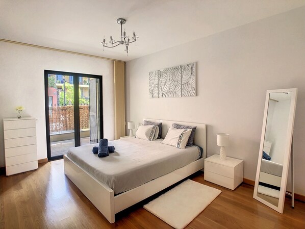 A modern bedroom with a bed, bedside tables, a mirror, and a chandelier.