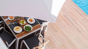 Een buitenterras met een tafel voor twee personen, omgeven door houten stoelen en een witte parasol.