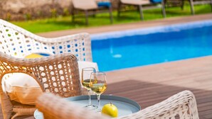 Een zwembadterras met rieten meubels, een tafel met glazen en een appel, en lounge stoelen op de achtergrond.