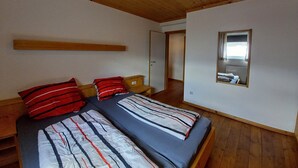 Una habitación con dos camas, vigas de madera en el techo, un espejo y una puerta que da a otra estancia.