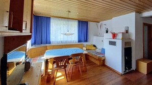 Habitación compacta y bien iluminada con techo de madera, zona de comedor con mesa y sillas, cama con colcha azul y una pequeña kitchenette con refrigerador y microondas.