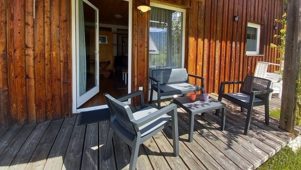 Una terraza de madera con mobiliario exterior y un ventanal que da al interior.
