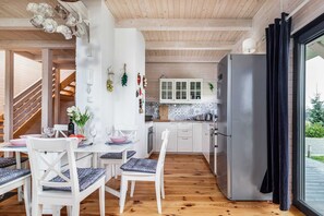 A modern kitchen with white cabinets, a stainless steel refrigerator, and a dining area with white chairs and a table set for two.