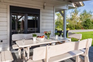 An outdoor patio with a wooden table and benches, surrounded by a white fence.