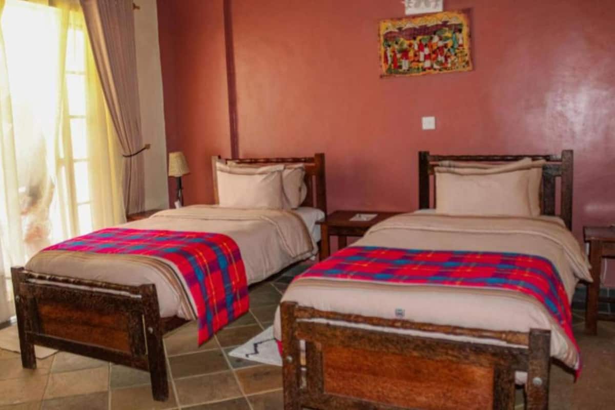 A room with two wooden beds, each with a colorful quilt. There is a small table and a lamp on one side.