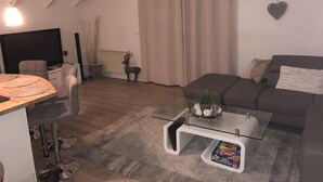 En moderne stue med et sofabord i glas, en sofa, et fjernsyn og et spiseområde med stole.
