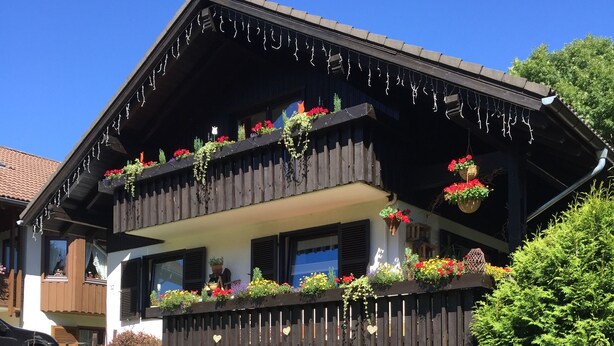 En toetagers chalet med en træbalkon pyntet med hængende planter og blomster.