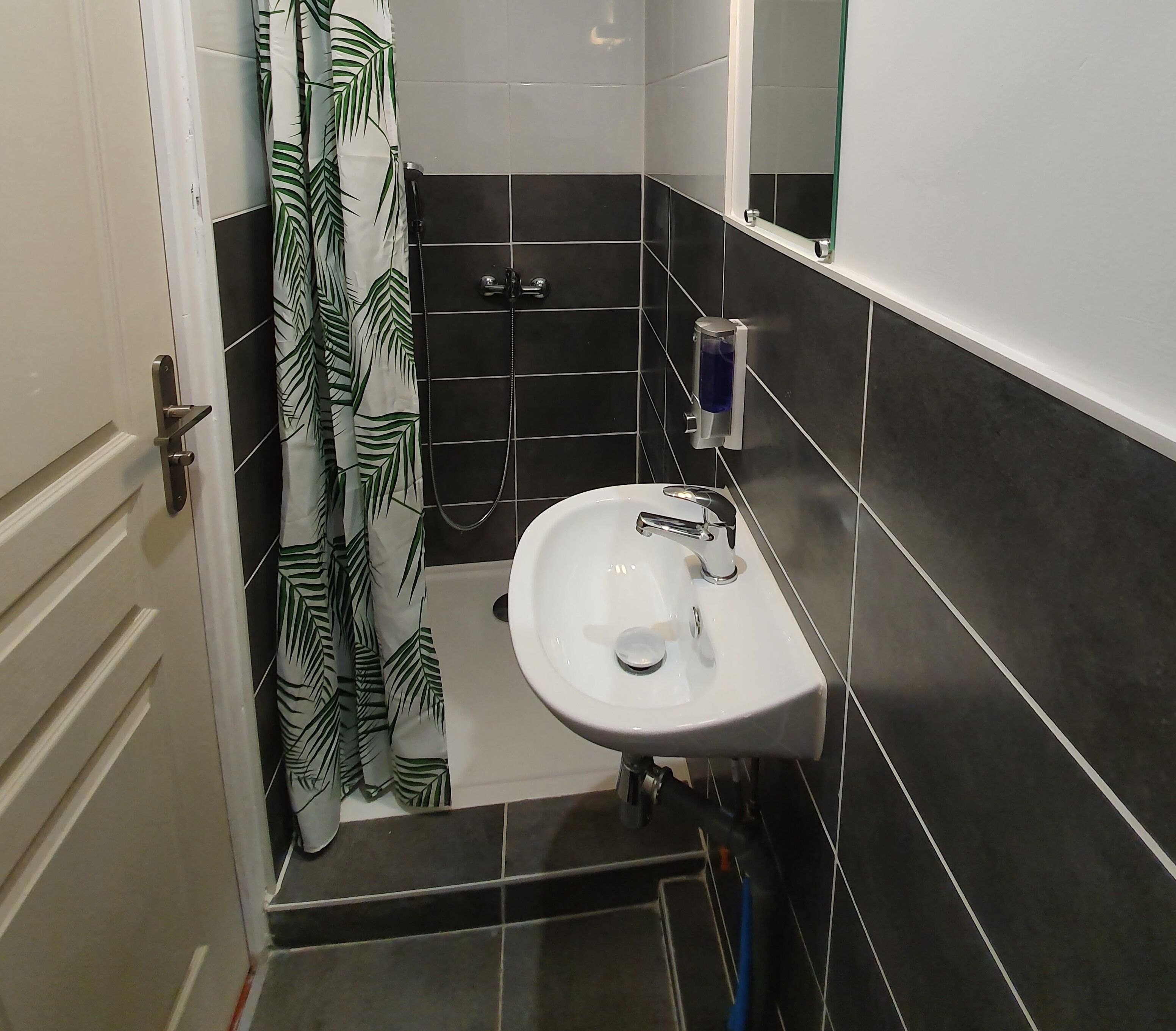 A bathroom with a white sink, black tiles, a shower, and a green leaf-patterned curtain.