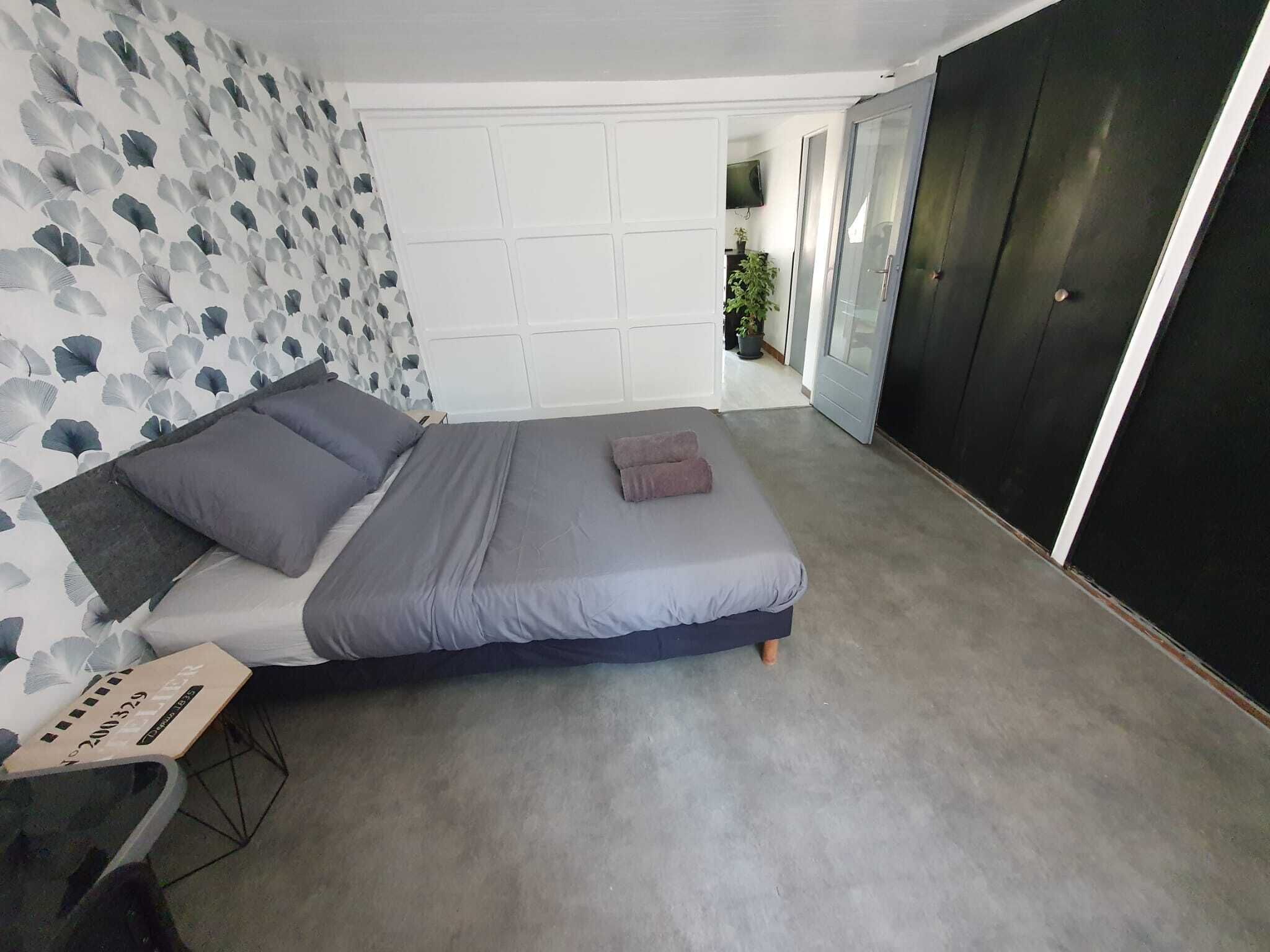 A modern bedroom with a bed, grey bedding, a desk with a chair, and a wardrobe.