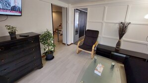 A modern office space with a glass coffee table, a black leather chair, a TV on the wall, and a potted plant. - NancyRoom (Vandœuvre-lès-Nancy)