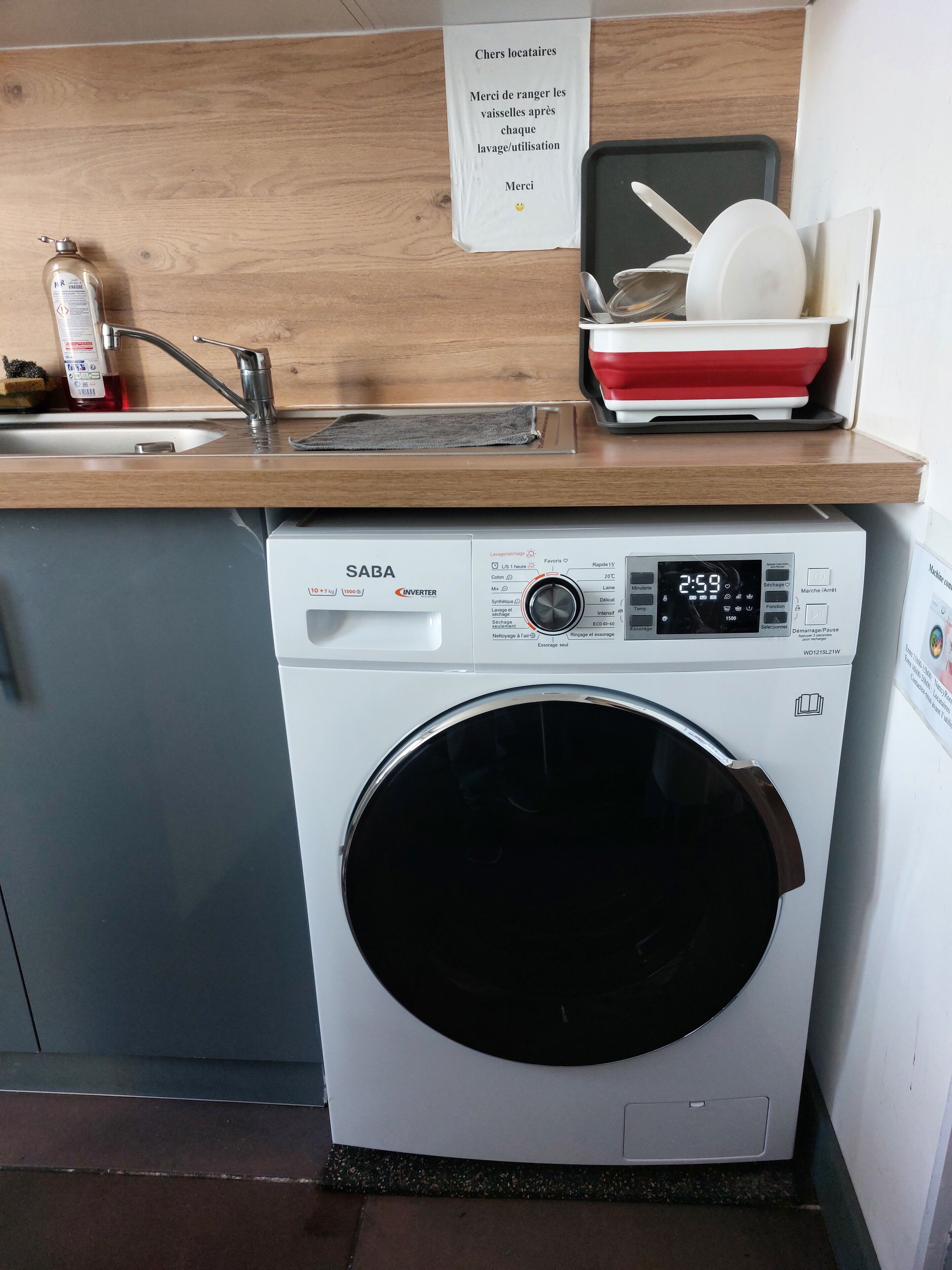 A SABA washing machine in a kitchen with a wooden countertop, a sink, and a sign above the machine.