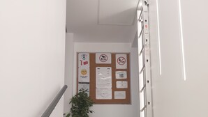 A staircase with a metal handrail, a potted plant, and a bulletin board with various notices. - NancyRoom (Vandœuvre-lès-Nancy)
