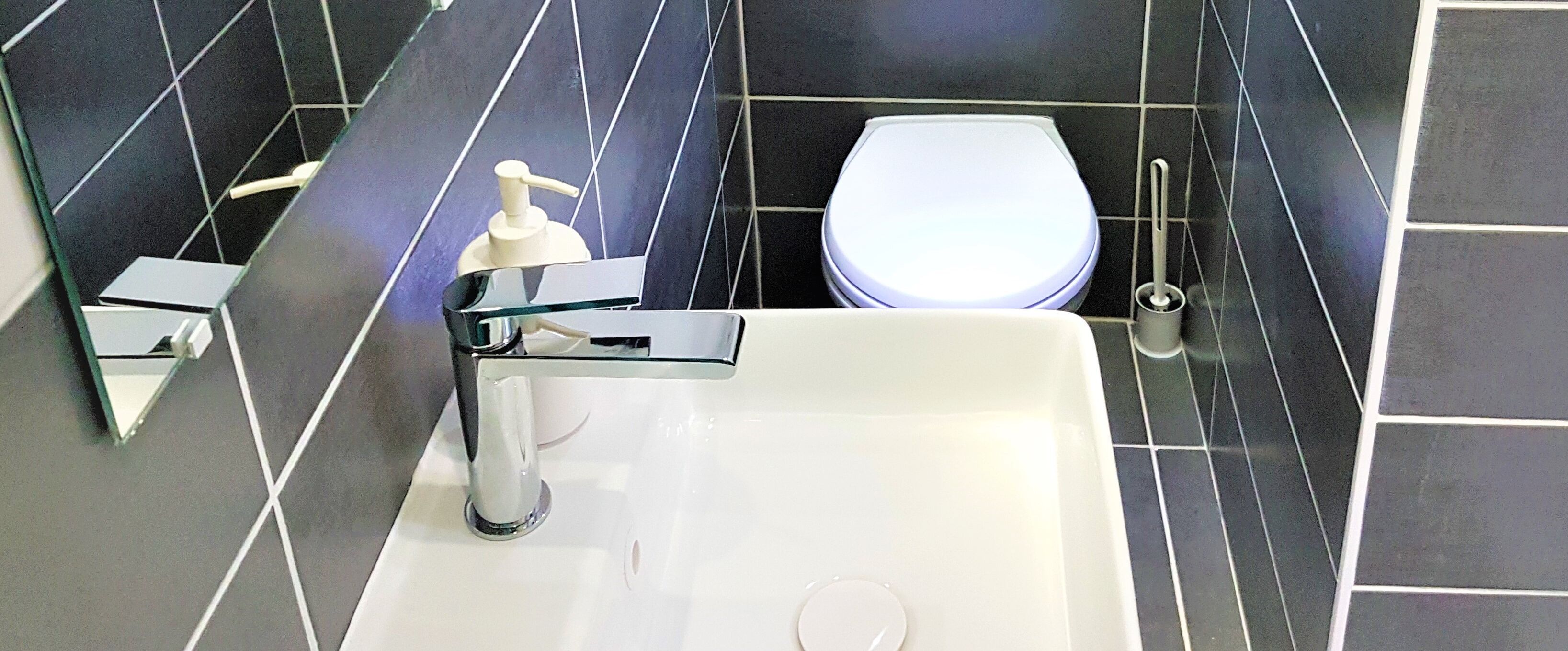 A bathroom with a white sink, a mirror, a toilet, and a hand soap dispenser.
