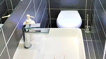 A bathroom with a white sink, a mirror, a toilet, and a hand soap dispenser.