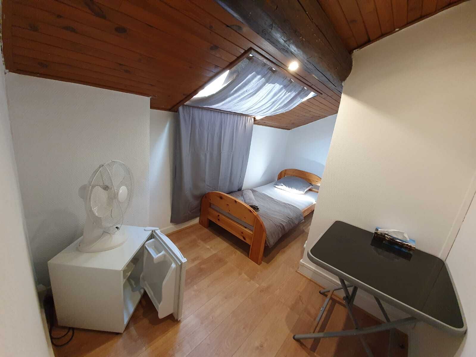 Una habitación pequeña y acogedora con techo de madera, una cama individual, un escritorio con silla y un ventilador de techo.