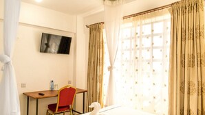 Habitación de hotel con cama, escritorio con silla, televisor en la pared y cortinas en las ventanas.