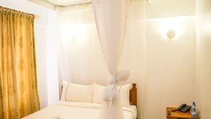 Una habitación de hotel con cama, mesita de noche con un teléfono y una botella, y una cortina.