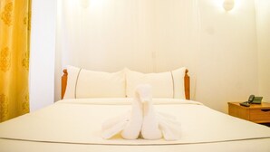 A hotel room with a neatly made bed, a bedside table with a lamp, and a curtain with a floral pattern. - Shadenet Hotel (Meru)