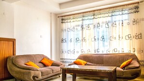 Una sala de estar con dos sofás y una mesa de centro, un aparador de madera y una ventana con cortinas estampadas.