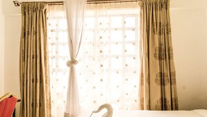 Una habitación de hotel con cama, una toalla con forma de cisne y cortinas de estampado floral.