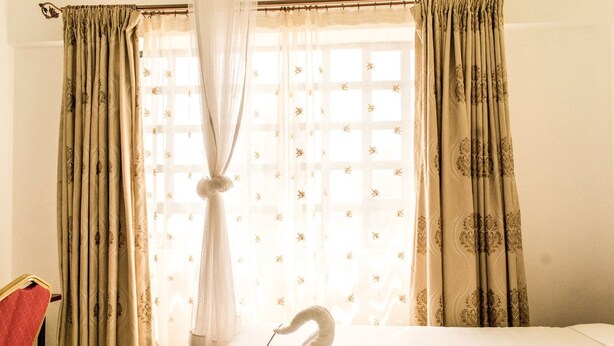 A hotel room with a bed, a swan-shaped towel, and curtains with a floral pattern. - Shadenet Hotel (Meru)