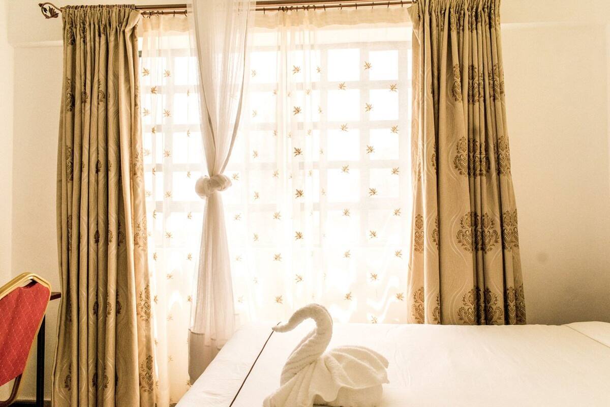 A hotel room with a bed, a swan-shaped towel, and curtains with a floral pattern.