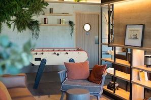 A cozy room with a foosball table, a comfortable chair with cushions, and a bookshelf with various items. - Campanile Saint-Brieuc Centre - Gare (Saint-Brieuc)