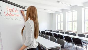 A person writing on a whiteboard in a conference room with rows of chairs and large windows.