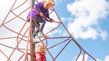 Dos niños trepando por una escalera de cuerda contra un cielo despejado.