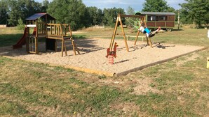 A playground with swings and a slide, surrounded by trees and a building in the background. - Cabin dinghy at anchor (Chassenard)