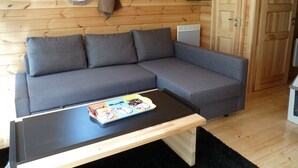 A modern log cabin interior with a grey sectional sofa, a wooden table with a board game, a round mirror, and a door. - Cabin dinghy at anchor (Chassenard)