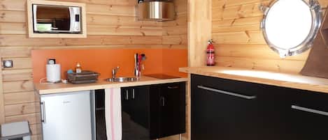 Una cocina compacta con microondas, lavamanos y un refrigerador pequeño.
