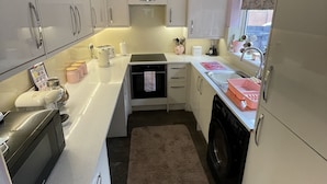 Cocina compacta con muebles blancos, horno empotrado, lavadora y ventana con una persiana con diseño de corazón.
