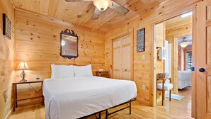A wooden cabin bedroom with a bed, bedside table, lamp, and a mirror on the wall. - Hot Tub, Mirror Lake Access, Log Cabin - Hawks Terrace by Carolina Properties (Lake Lure)