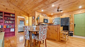 A wooden cabin interior with a dining area, kitchen, and a green door. - Hot Tub, Mirror Lake Access, Log Cabin - Hawks Terrace by Carolina Properties (Lake Lure)