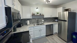 A modern kitchen with white cabinets, stainless steel appliances, and a grey backsplash.