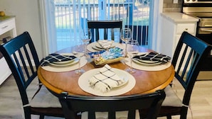 A dining area with a round table set for four, surrounded by chairs. There are wine glasses and a basket of snacks on the table.