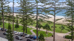 Ein Parkplatz mit Autos, einer Grünfläche und Blick auf Strand und Meer.