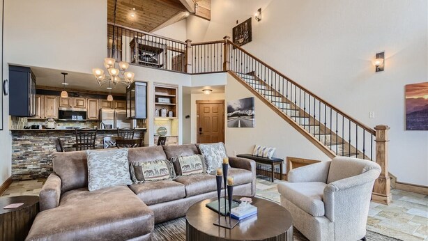 A spacious living area with a large brown leather sofa, a beige armchair, and a round coffee table. A wooden staircase with a railing leads to an upper level. - Well Maintained 2 Bedroom Plus Loft Condo close to Lake Dillon!! (Frisco)
