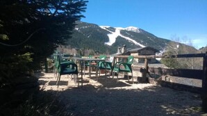 An outdoor seating area with tables and chairs, a wooden fence, and a mountain backdrop. - Hotel Roc de St Miquel (Soldeu)