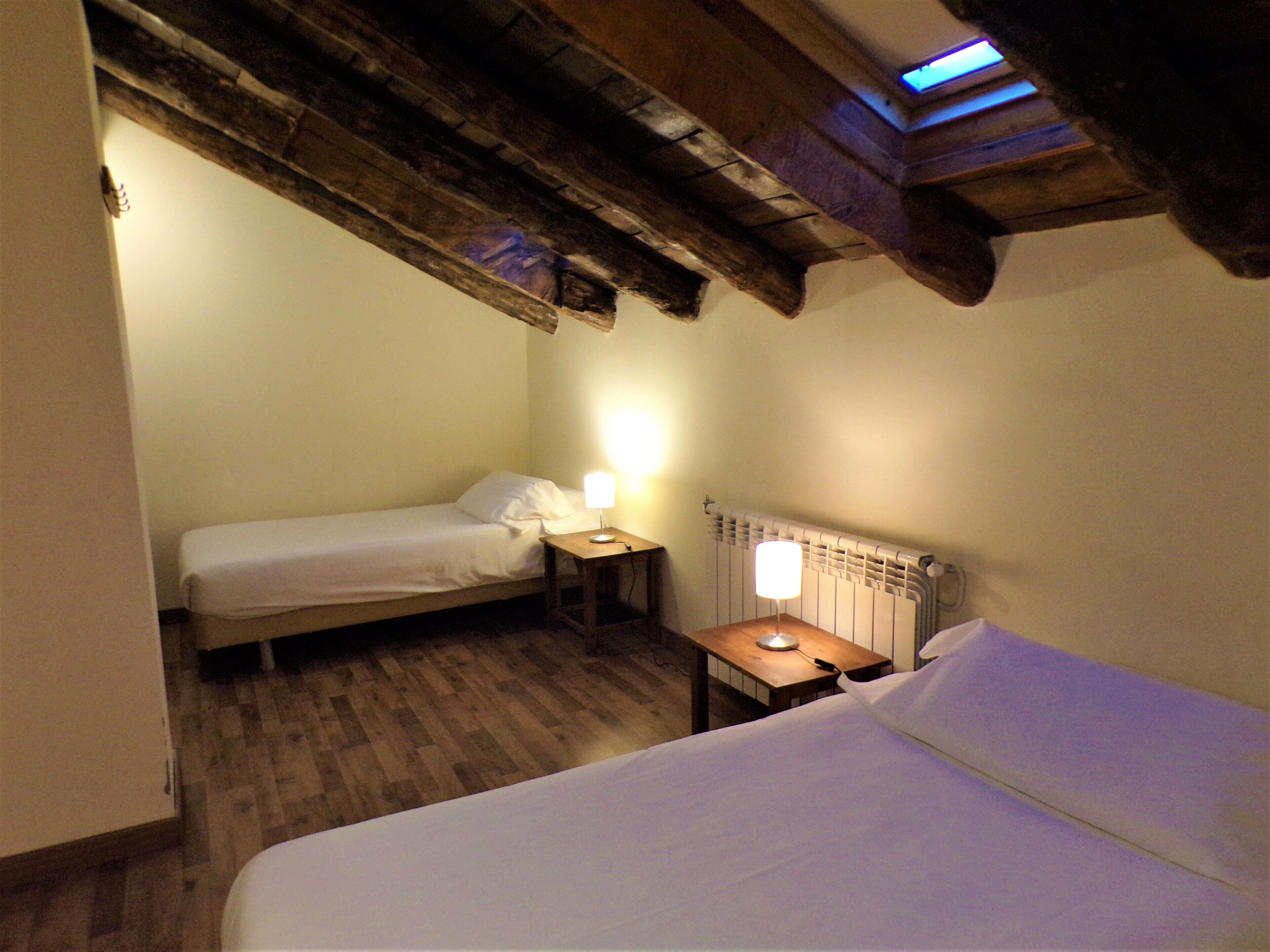 A small, cozy room with two beds, a wooden ceiling, and a radiator.