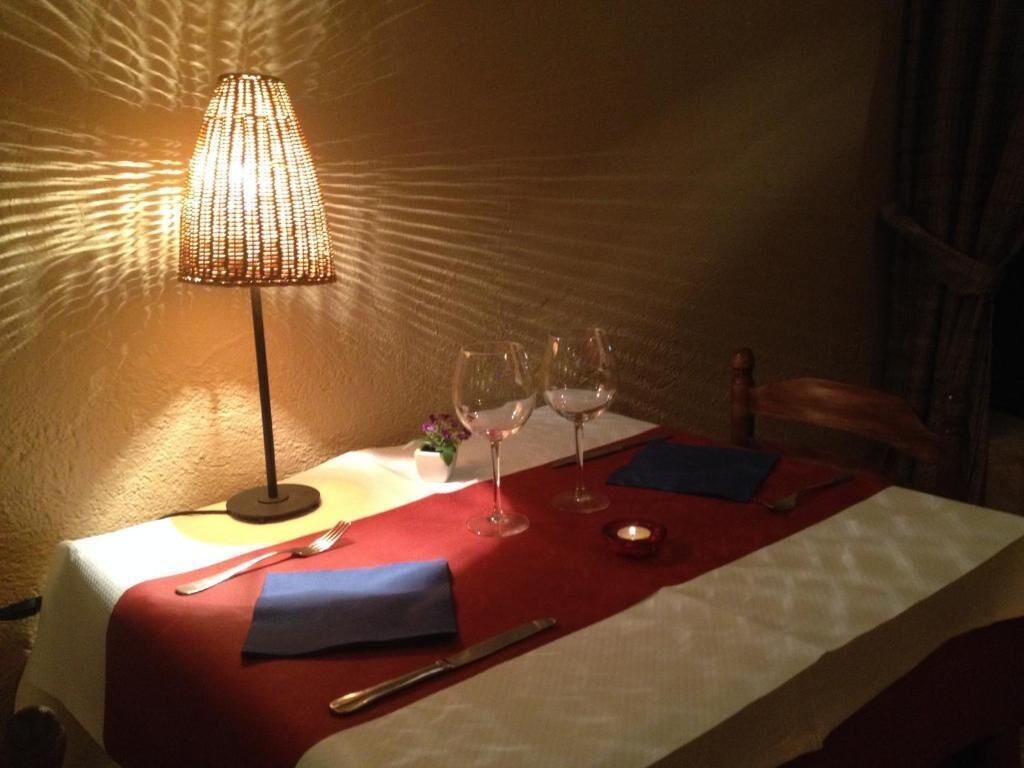 Une table à manger dressée avec une nappe rouge, une bougie et deux verres à vin.