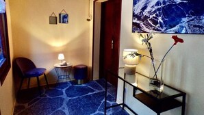 A hallway with a blue patterned carpet, a small round table with a lamp, a chair, and a framed picture on the wall. - Hotel Roc de St Miquel (Soldeu)